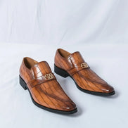 Brown leather shoes with a crocodile pattern worn by a person on a light gray background