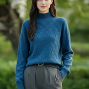 A woman wearing a textured blue mock-neck knit sweater with a checkerboard pattern, paired with dark gray trousers