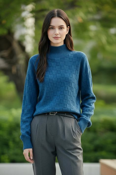A woman wearing a textured blue mock-neck knit sweater with a checkerboard pattern, paired with dark gray trousers