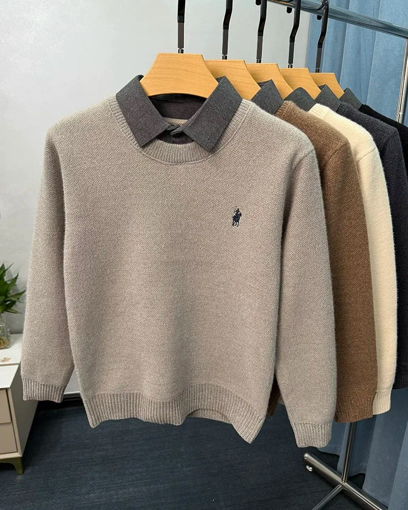 Beige sweater with a collar and logo on a hanger against a white wall.
