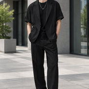 A black short-sleeve blazer styled over a black t-shirt with a silver necklace, shown against a plain white background.