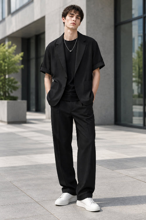 A black short-sleeve blazer styled over a black t-shirt with a silver necklace, shown against a plain white background.