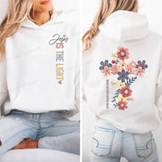 A white pullover hoodie shown on a model from the front and back. The front features the text 'Jesus IS THE LIGHT' in black, gray, and gold.