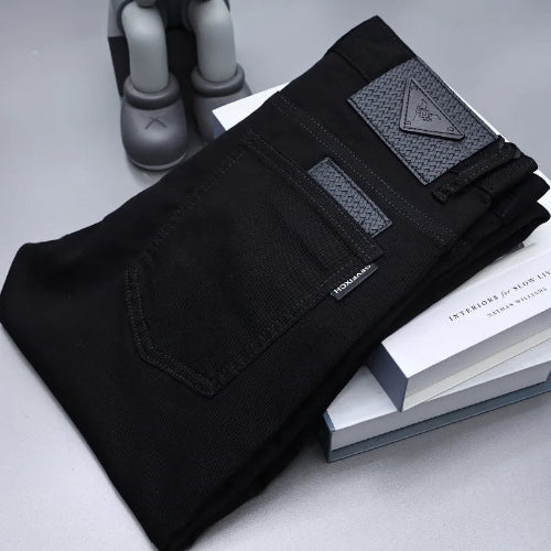 Black denim jeans folded on top of stacked white books, with a gray sculptural object in the background. 