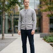 A light gray knit cardigan sweater with a round neckline, front button closure, and ribbed cuffs and hem, hanging on a dark wooden hanger against a dark gray background.