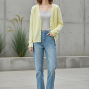 A woman wearing a soft pastel yellow cardigan sweater over a light gray top and blue jeans, 