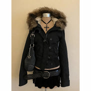 A black hooded jacket with a brown fur-trimmed hood, displayed on a mannequin torso with a black skirt, braided belt, denim bag, and cross necklace against a plain beige background.