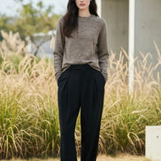 A woman wearing a light brown knit crewneck sweater, shown from the waist up 