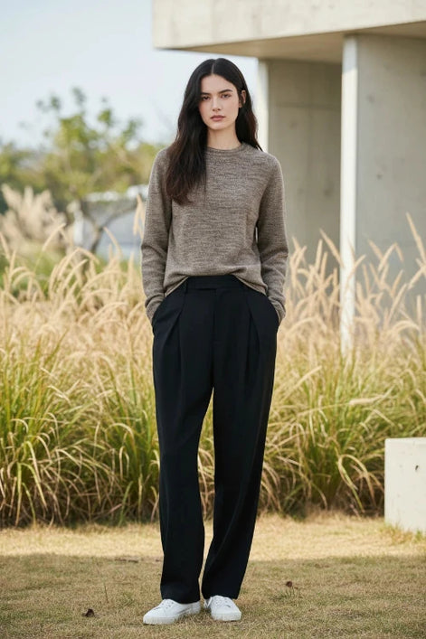 A woman wearing a light brown knit crewneck sweater, shown from the waist up 