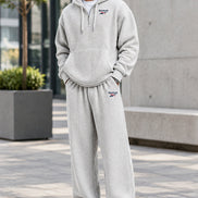 A man wearing a light gray waffle-knit Reebok tracksuit, featuring a pullover hoodie and matching sweatpants, against a plain white background.