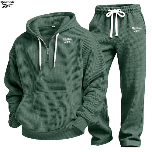 A dark green waffle-knit two-piece tracksuit set by Reebok, featuring a pullover hoodie with a half-zip neckline and matching jogger pants 