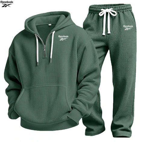 A dark green waffle-knit two-piece tracksuit set by Reebok, featuring a pullover hoodie with a half-zip neckline and matching jogger pants 