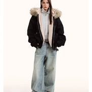 Person wearing a black coat with fur hood, light shirt, and blue jeans on a white background