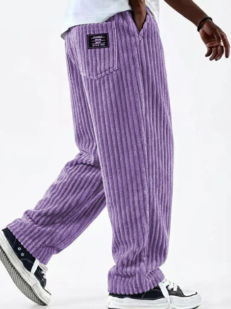 Purple corduroy pants worn by a person on a white background