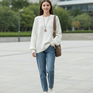 A woman wearing a cream-colored cable-knit sweater with textured diamond patterns, 