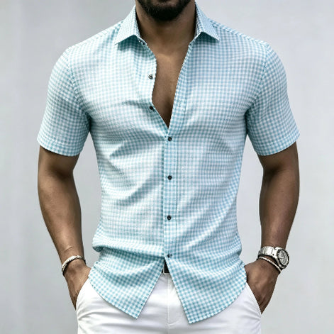 A man wearing a light blue and white gingham short-sleeve button-up shirt with white pants, 