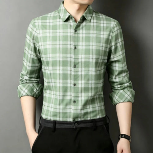 A man wearing a green and white plaid long-sleeve button-up shirt with black trousers, shown from the chin down against a dark gray background.