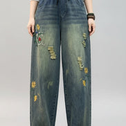 Person wearing blue jeans with floral embroidery in a minimal indoor setting.