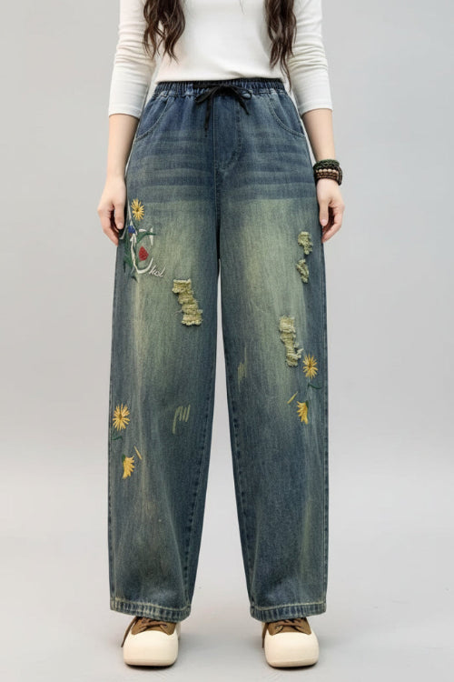 Person wearing blue jeans with floral embroidery in a minimal indoor setting.