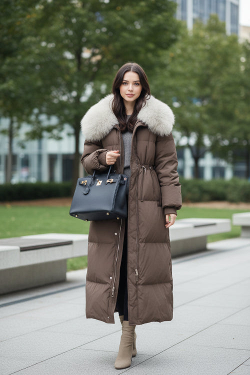 A woman takes a mirror selfie in a clothing store while wearing a long brown puffer coat 