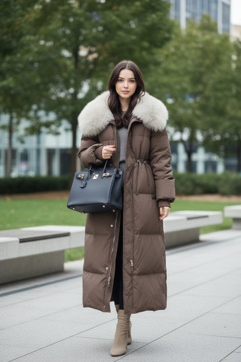 A woman takes a mirror selfie in a clothing store while wearing a long brown puffer coat 