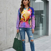 A woman wearing a vibrant, multicolored long-sleeve sweatshirt with a large floral print, paired with blue jeans, holding a bouquet of white roses.