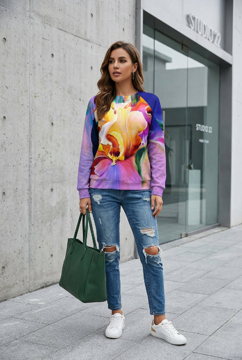 A woman wearing a vibrant, multicolored long-sleeve sweatshirt with a large floral print, paired with blue jeans, holding a bouquet of white roses.