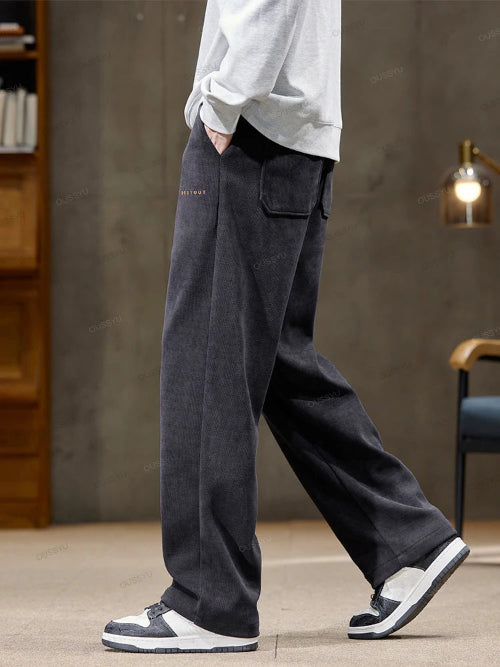 Person wearing dark gray pants with a visible brand logo, standing indoors.