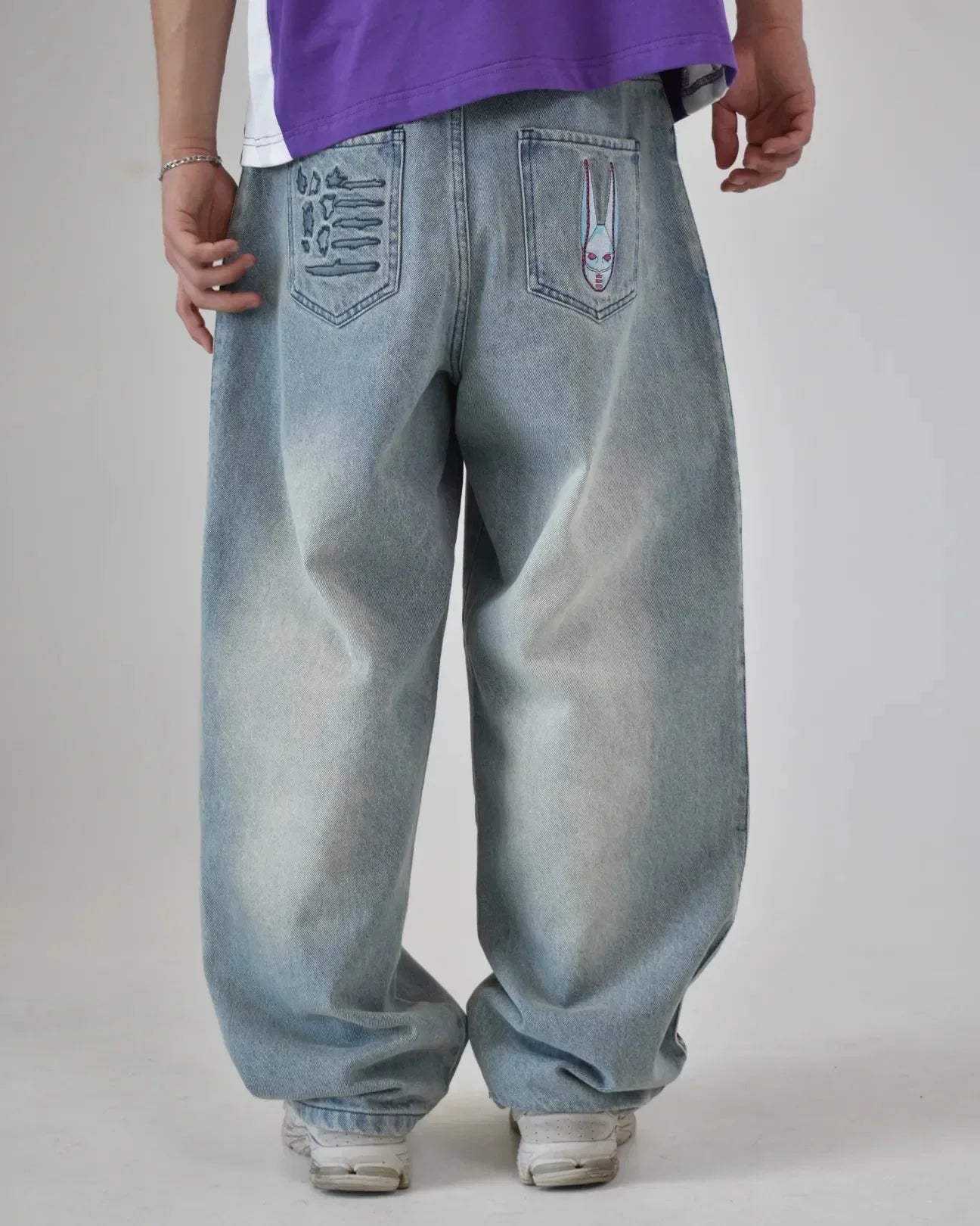 Person wearing light blue baggy jeans with unique designs on the pockets against a plain background