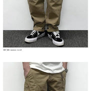 Two front-angle views of a model wearing khaki loose-fit cargo pants, showing large flap thigh pockets, curved seam detailing, and stitched knee panels.