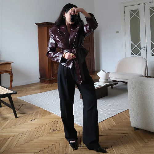 Woman taking a full-length mirror photo wearing a glossy dark brown belted jacket with wide lapels and black wide-leg trousers
