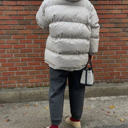 A person viewed from behind wearing a light gray puffer jacket, dark gray pants, and beige slip-on shoes, 