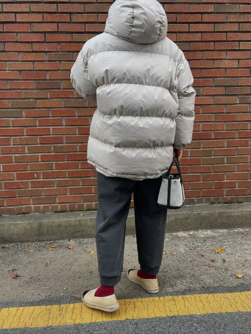 A person viewed from behind wearing a light gray puffer jacket, dark gray pants, and beige slip-on shoes, 