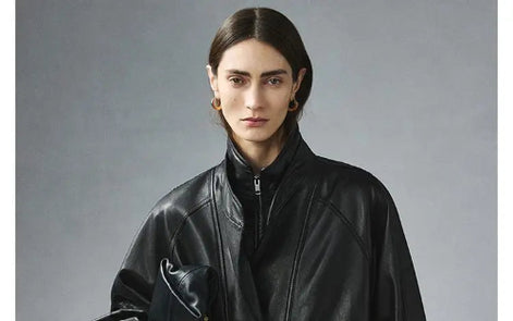 Close-up front view of a woman wearing a black faux leather jacket with a zipped inner collar and layered outer collar against a gray background