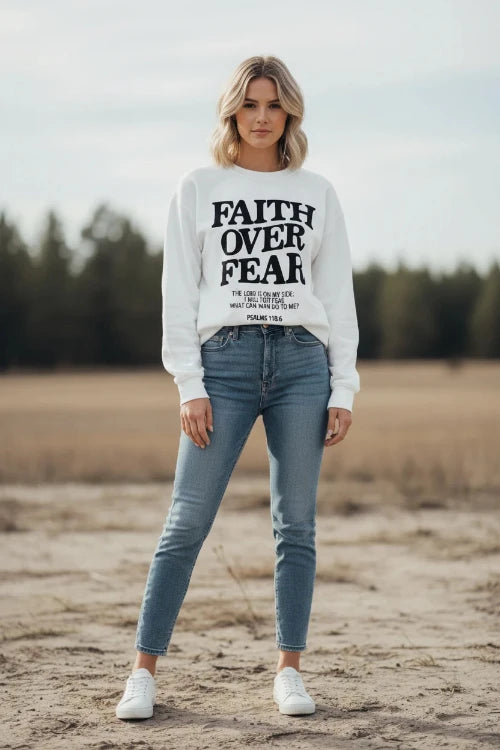 White sweatshirt with 'Faith Over Fear' text on a wooden background
