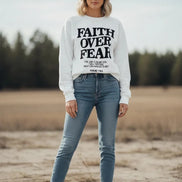 White sweatshirt with 'Faith Over Fear' text on a wooden background