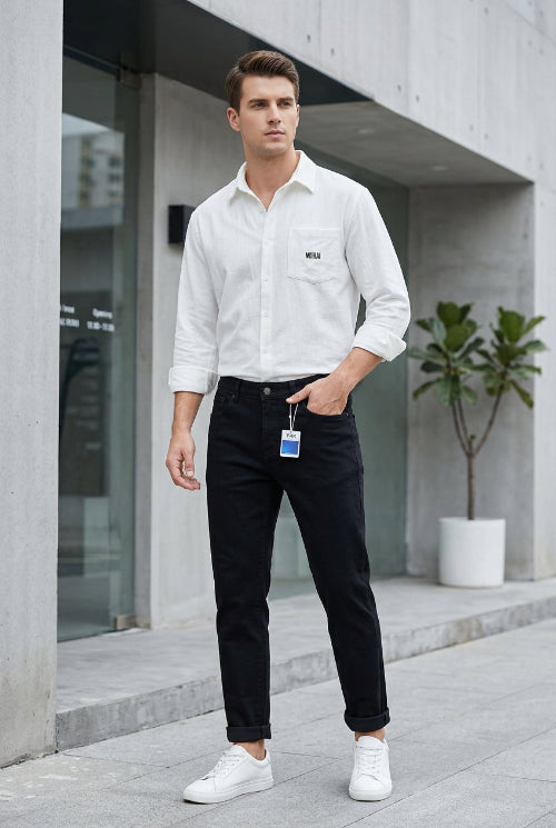 Black slim-fit jeans hanging on a metal rack, displayed alongside a white button-up shirt in a styled retail setting with a gray wall, floor lamp, plant, and storage boxes.
