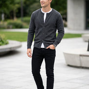 A dark gray knit cardigan sweater hanging on a wooden hanger against a dark gray background.