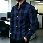 A man wearing a long-sleeve button-up shirt with a navy and black buffalo plaid pattern, standing in an office environment.