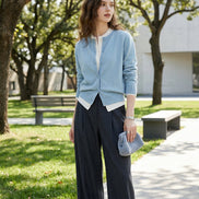 Person wearing a light blue cardigan over a white shirt with dark pants in an indoor setting.