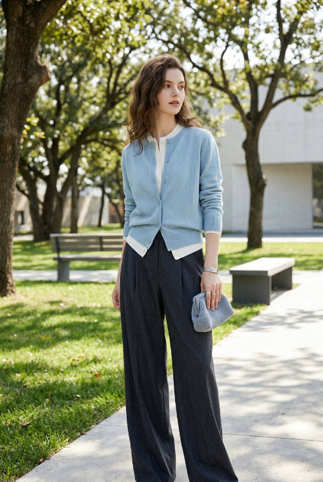 Person wearing a light blue cardigan over a white shirt with dark pants in an indoor setting.