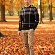 Person wearing a black and beige plaid sweater against a dark background