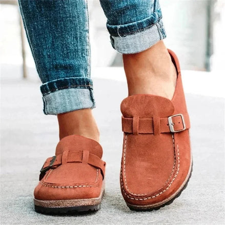 Brown loafers with buckles worn with rolled-up jeans on a light background