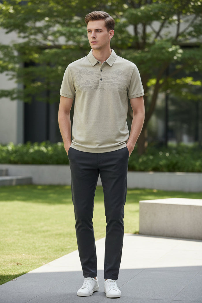 A close-up of a beige short-sleeve polo shirt on a black hanger, held by a hand to show the fabric texture. The shirt features a subtle landscape pattern on the front and a small circular logo on the chest pocket.