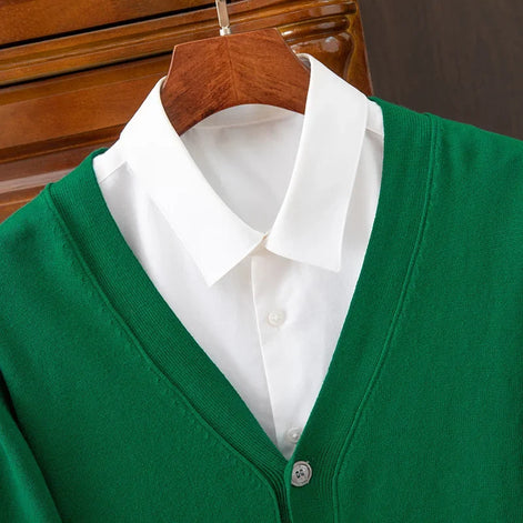 Green cardigan over a white shirt on a wooden hanger against a dark background
