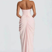 A woman viewed from the back wearing a pale blush pink strapless gown with a corset-style back and gathered skirt, 