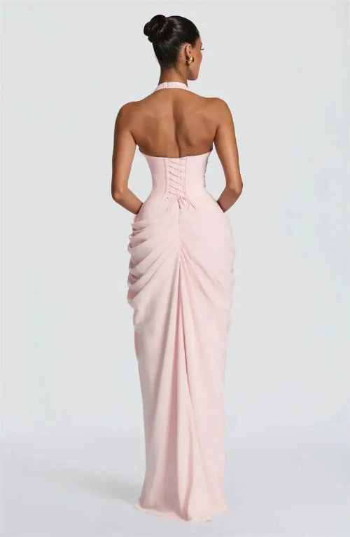 A woman viewed from the back wearing a pale blush pink strapless gown with a corset-style back and gathered skirt, 