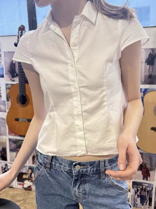 Front view of a white short-sleeve blouse with a pointed collar, button front, and shaped waist, paired with blue jeans