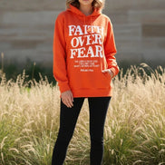 Orange hoodie with 'Faith Over Fear' text on a wooden surface