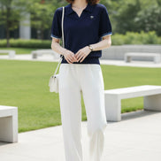 A woman wearing a navy blue short-sleeve polo shirt with a textured knit fabric, a small bow pin on the chest, and striped trim on the collar and sleeve cuffs, paired with white bottoms.